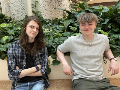 Portræt af Karl og Aksel, sidder sammen på en bænk med grønne planter i baggrunden