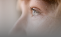 Nærbillede, udsnit af ung kvindes ansigt i profil, lettere sløret, fokus på øje.